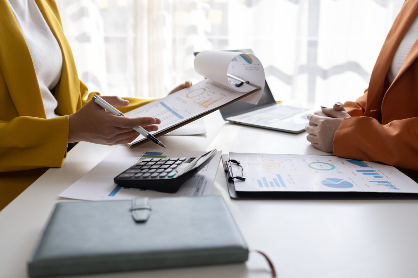 Two people working on financial documents at a desk with a calculator and laptop.