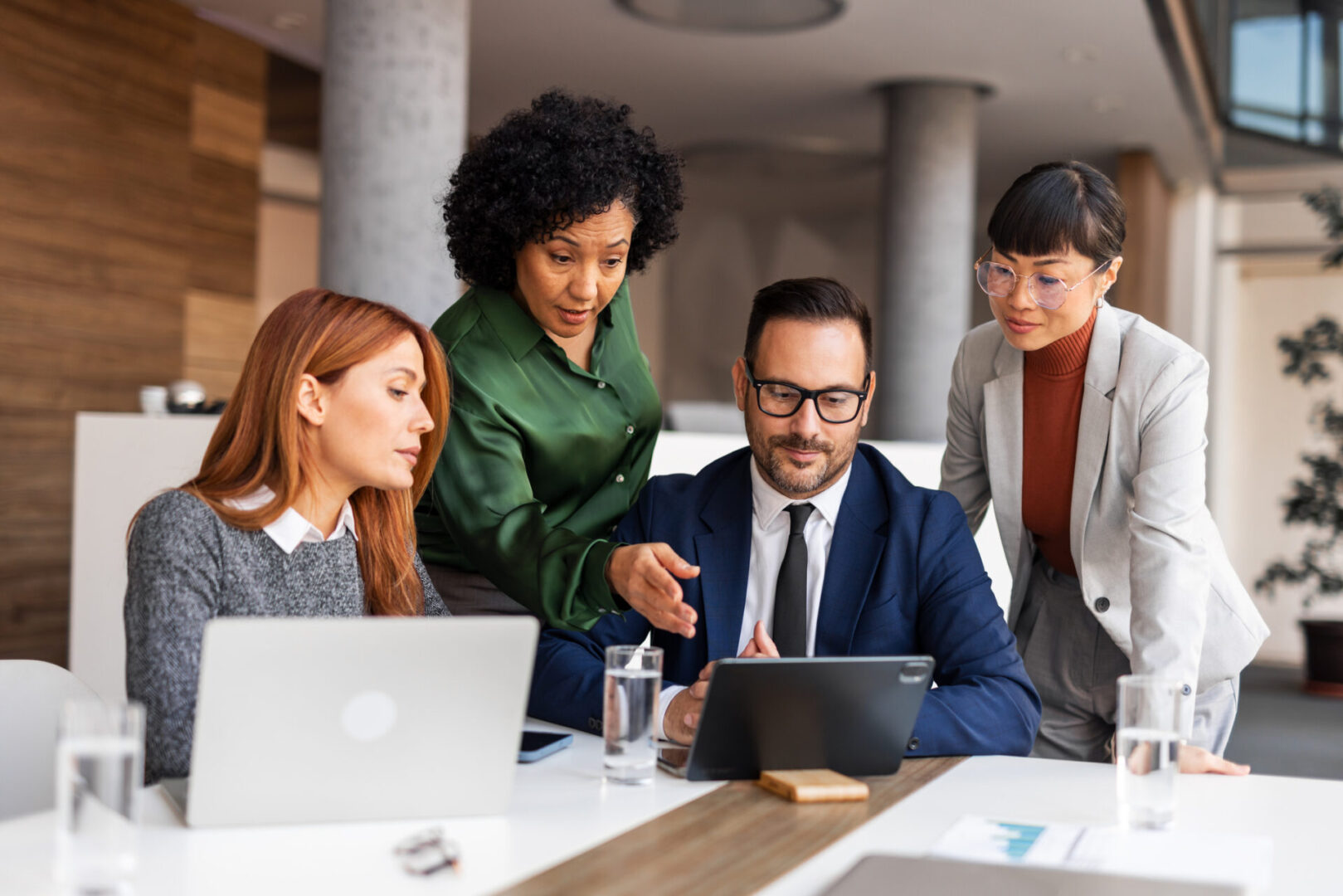 Four professionals collaborating around a tablet in a modern office.
