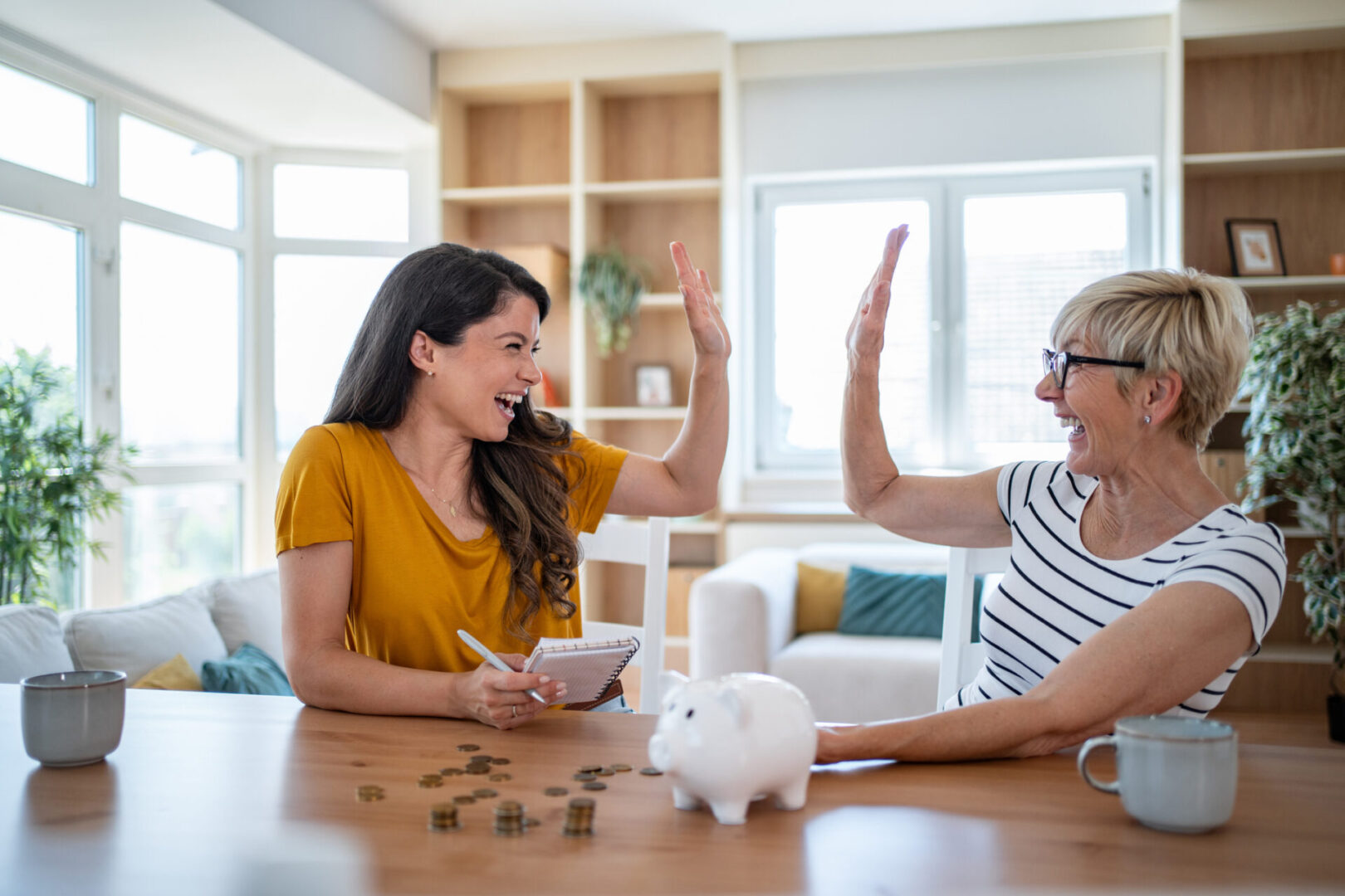 Two women happily discussing finances with a piggy bank on the table.