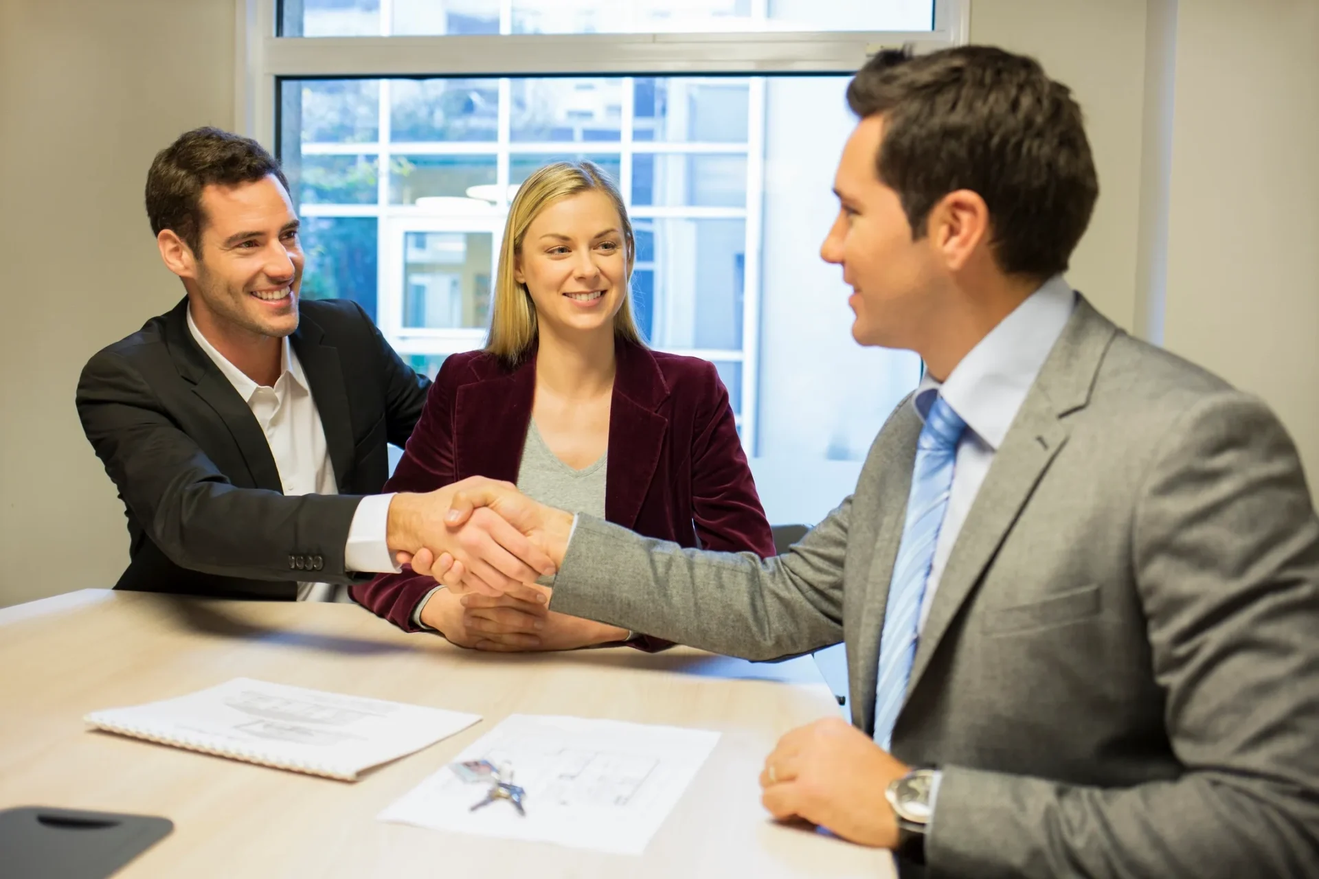 Two men shaking hands in a business meeting with a woman smiling.