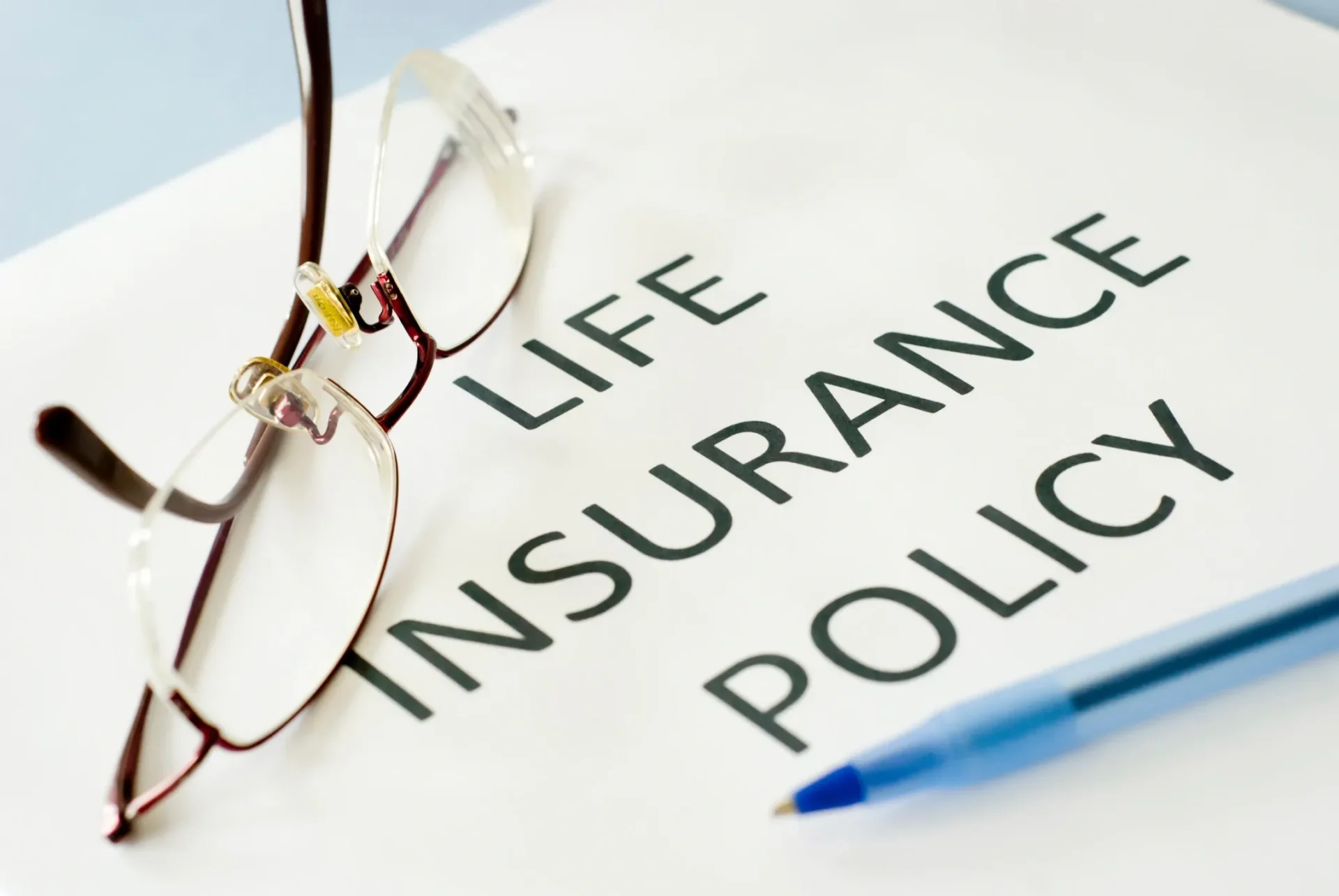 A pair of glasses and a pen resting on a life insurance policy document.