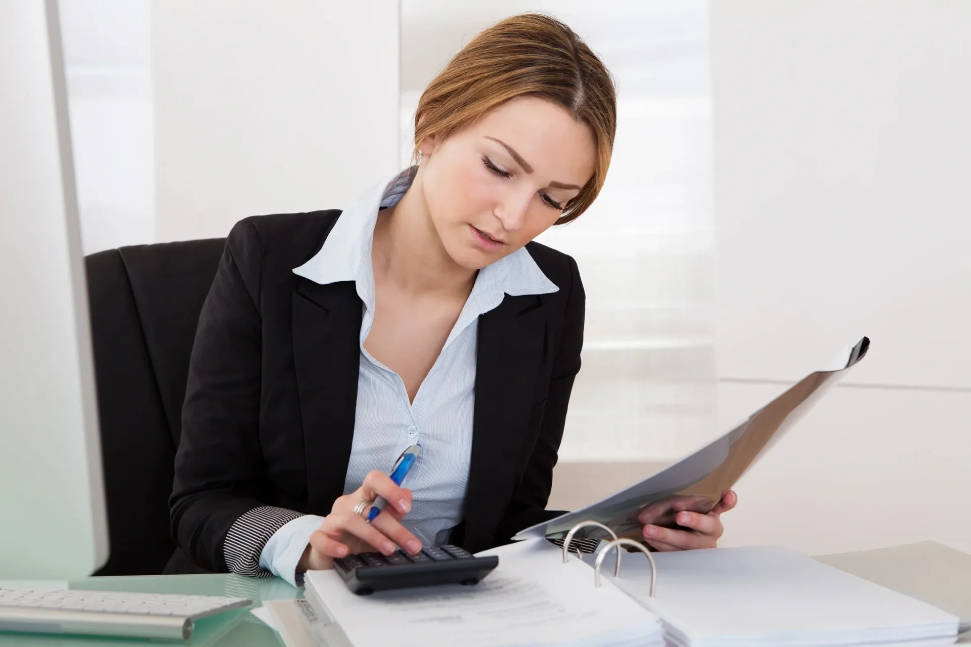 A businesswoman calculating finances using a calculator and documents.