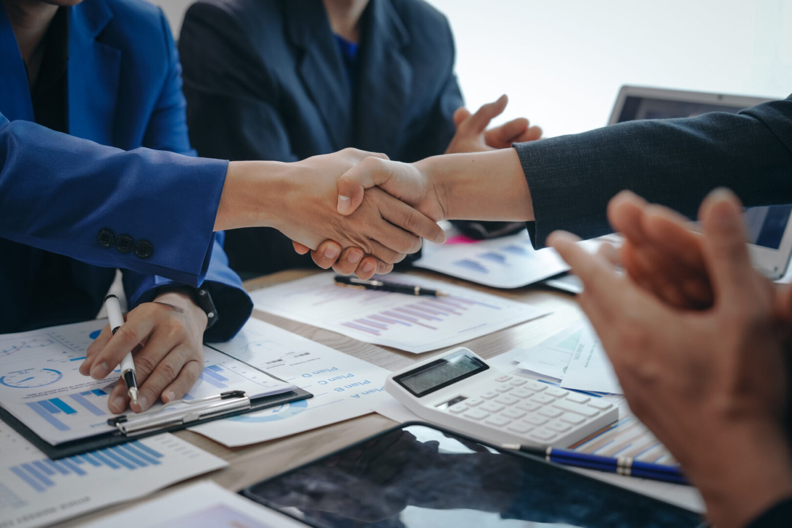 Business handshake sealing a deal over documents and devices.