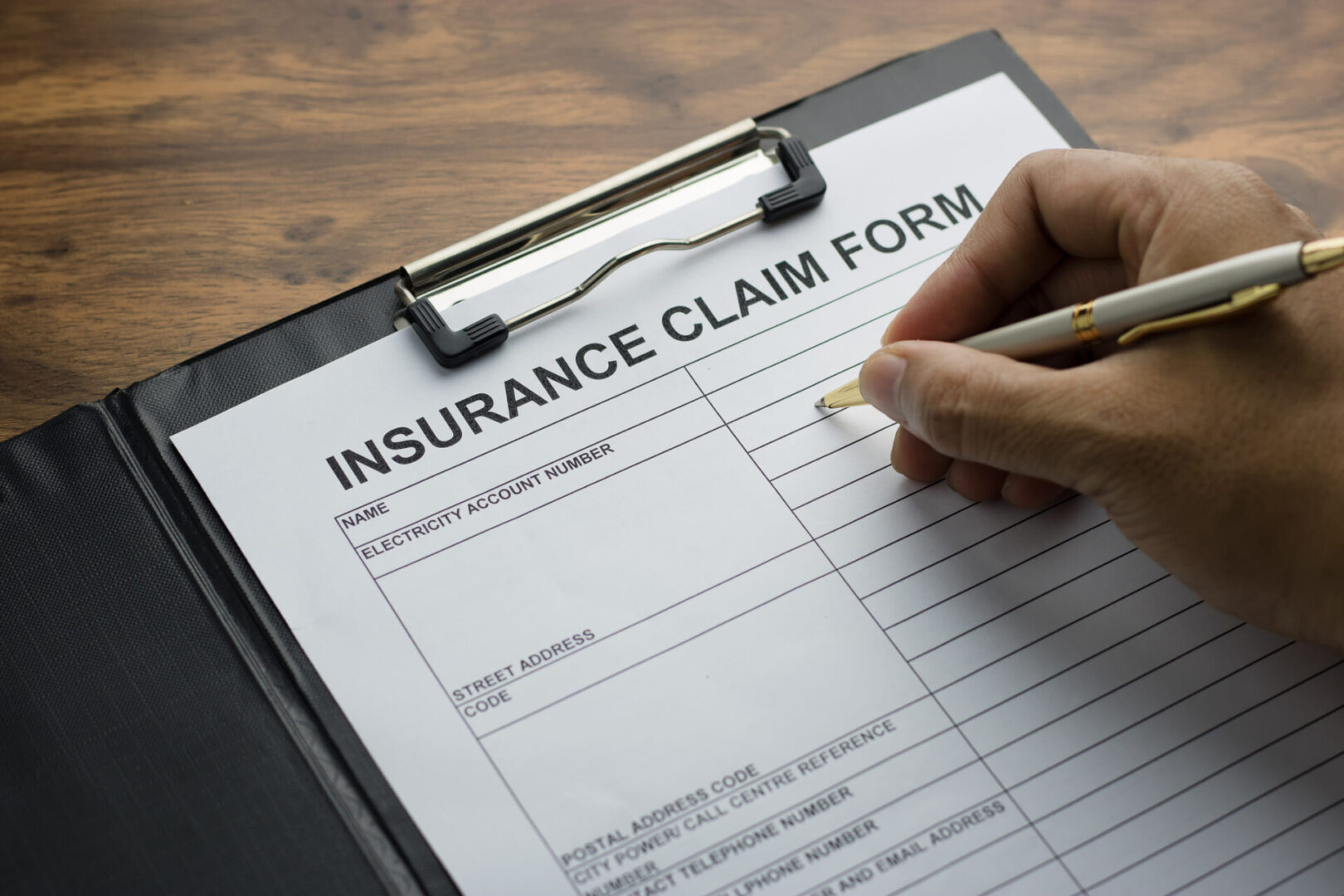 Person filling out an insurance claim form on a clipboard.