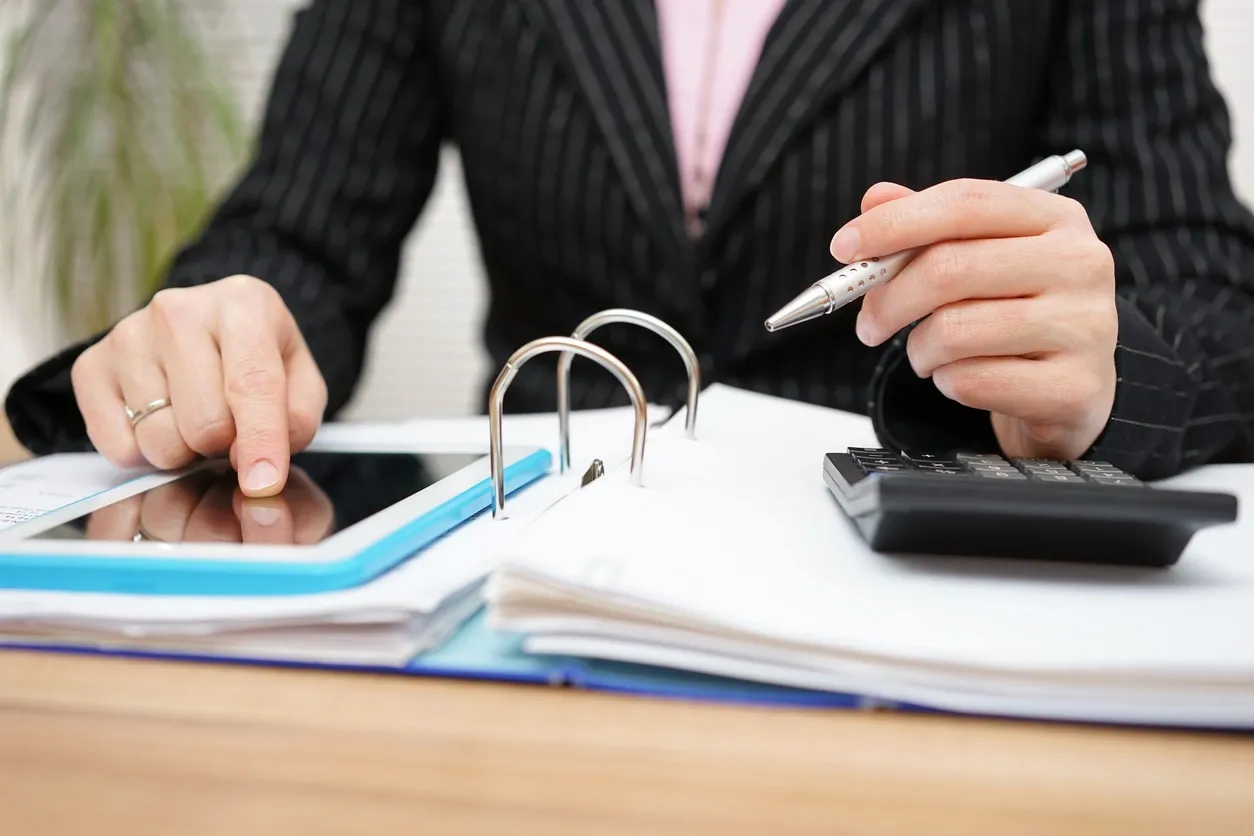 Person using calculator and reviewing documents at desk.