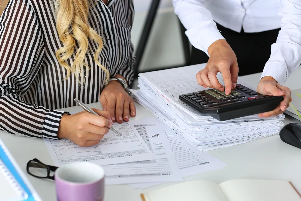 Two people analyzing financial documents with a calculator.