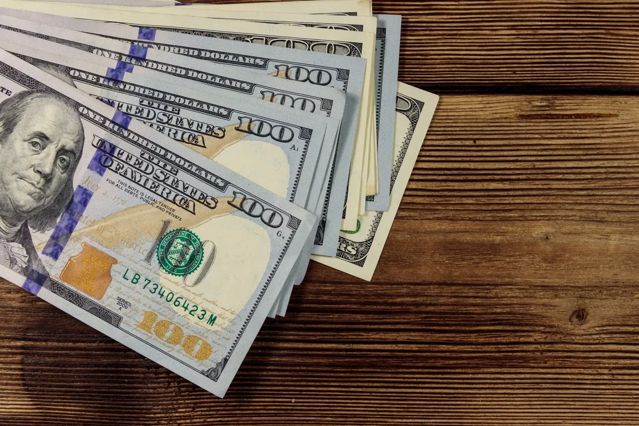 Stack of US hundred-dollar bills on a wooden surface.