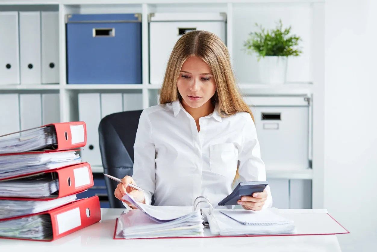 Woman working with documents and calculator at desk.